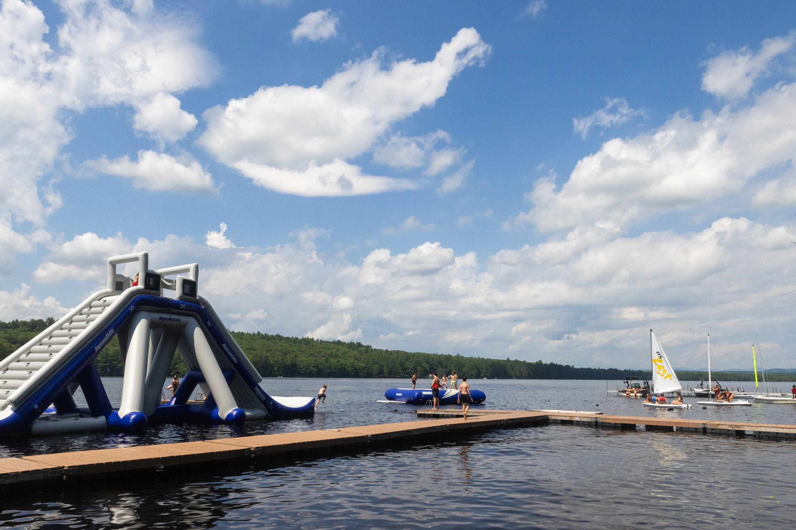 The Camp Kingswood waterfront on a bright afternoon, the water slide on the dock and sailboats out on the lake