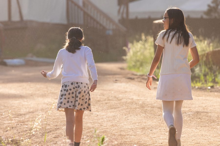 Two campers in white walking a sunlit path at Ramah in the Rockies